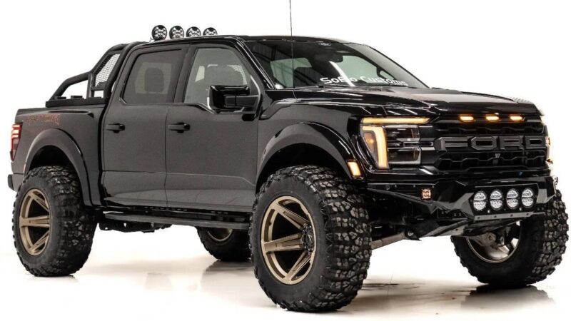A black Ford Raptor pickup truck with large off-road tires, aftermarket wheels, and additional LED lights showcases the capability expected from luxury trucks, all photographed in a studio setting.