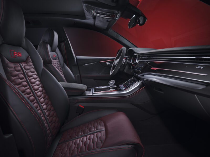 Interior view of the 2025 Audi RS Q8 Performance, featuring black and red leather seats with red stitching, digital displays, and "RS" branding on the headrests. Review: Experience luxury craftsmanship and cutting-edge tech inside.