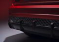 Close-up of the rear bumper and exhaust area of a red Audi RS Q8, featuring black detailing and part of a license plate. Review: 2025 Audi RS Q8 Performance highlights its striking design elements.