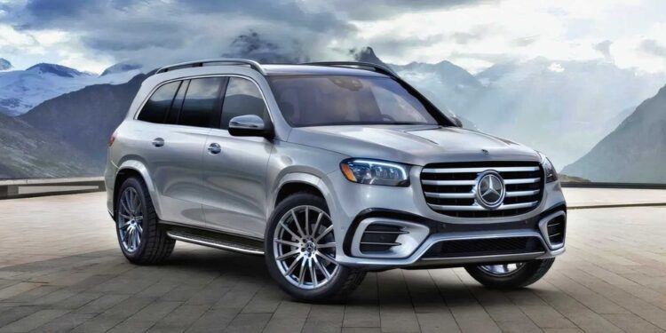 A silver Mercedes-Benz SUV, featured in the Review: 2025 Mercedes-Benz GLS 580 4Matic, is parked on a stone pavement with mountains and cloudy skies in the background.