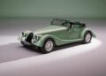 A classic-style Morgan Plus Four convertible sports car with round headlights and chrome accents is parked indoors under soft lighting, celebrating the 75th Anniversary of the iconic Morgan legacy.