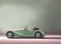 A light green Morgan Plus Four roadster convertible is shown in profile against a neutral gradient background, celebrating the Morgan anniversary in timeless style.