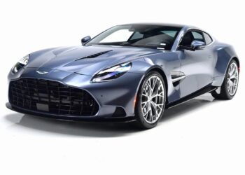 A blue Aston Martin Vanquish coupe sports car with a powerful V12 engine is parked in a studio with a white background, viewed from the front left angle.