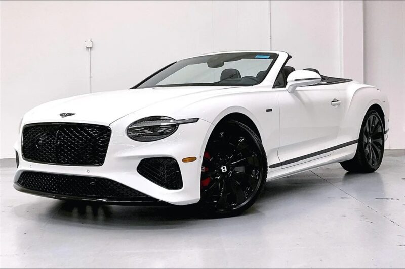 A white exotic luxury car convertible with a black grille and wheels is parked indoors on a light gray floor against a plain white wall.