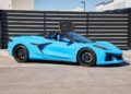 A bright blue luxury convertible sports car parked in front of a striped black fence and a sign reading “Vegas Auto Gallery”—the perfect exotic car for sale.