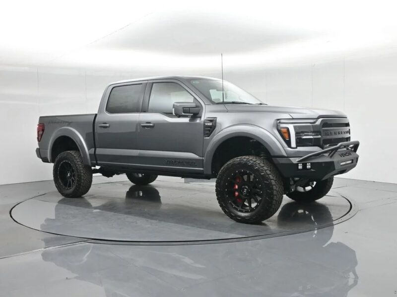 A gray lifted pickup truck with large off-road tires, black rims, and aftermarket front bumper embodies both style and rugged performance, displayed in a white indoor studio.