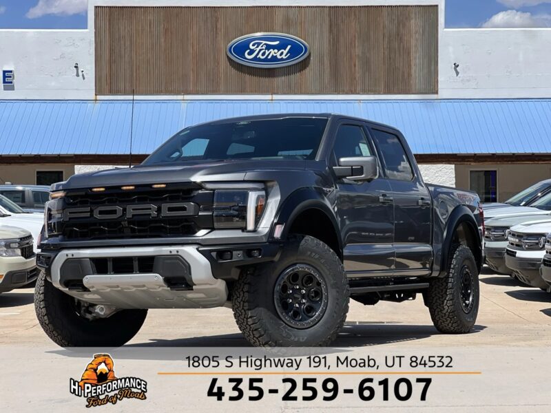 A black Ford pickup truck, known for its comfort and style, is parked in front of a Ford dealership under a blue sky. Other vehicles are visible in the background along with the dealership address and phone number.