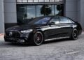 A luxury car, this black Mercedes-Benz sedan is parked in front of a modern building on a concrete surface.