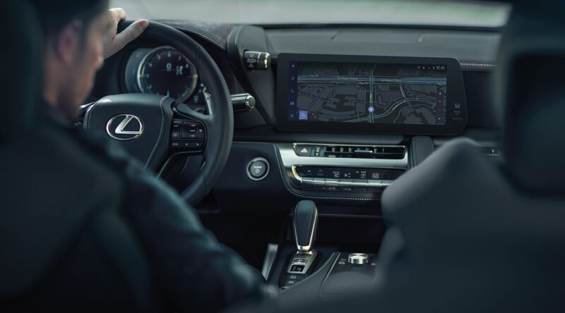 A person sits in the driver's seat of a Lexus, hands on the steering wheel and navigation map glowing on the center screen—capturing the sleek luxury showcased in our Review: 2025 Lexus LC 500 Convertible.