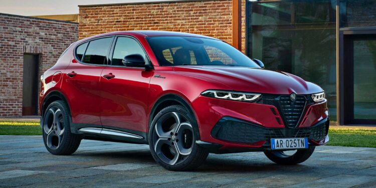A red 2026 Alfa Romeo Tonale hybrid SUV is parked on a stone driveway in front of a modern brick and glass building.