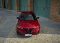 A red Alfa Romeo Tonale with sharper handling is parked on a cobblestone street in front of a brick building with teal doors, reflecting the spirit of the 2026 update.