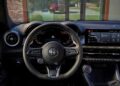 A view of a modern car interior showing the steering wheel with the Alfa Romeo logo, a digital instrument cluster, and a center touchscreen display—highlighting the 2026 Alfa Romeo Tonale with advanced hybrid power.