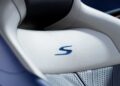Close-up of a light gray Aston Martin car seat with a blue "S" logo stitched into the leather upholstery, reminiscent of the DB12 S Super Tourers.