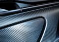 Close-up of an Aston Martin DB12 S interior door panel featuring a Bowers & Wilkins speaker with a perforated metallic grille and carbon fiber trim, showcasing the luxury expected from Super Tourers.