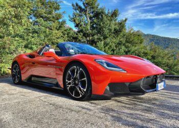 A 2026 Maserati MCPura Cielo First Drive red convertible sports car is parked on a concrete surface near trees and mountains under a blue sky.