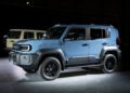 A blue 2026 Toyota Land Cruiser FJ compact SUV is displayed indoors under bright lighting, projecting a capable and rugged stance, with a beige SUV visible in the background.
