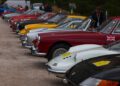 A lineup of classic sports cars, including a few from the Ferrari Cavalcade, parked in a row at an outdoor event in South Tyrol, with one person standing near the vehicles.
