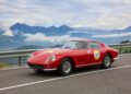 A red classic Ferrari sports car with the number 27 drives on a mountain road in South Tyrol, offering a scenic view of distant peaks and clouds—an iconic moment reminiscent of Italy’s celebrated Ferrari Cavalcade.
