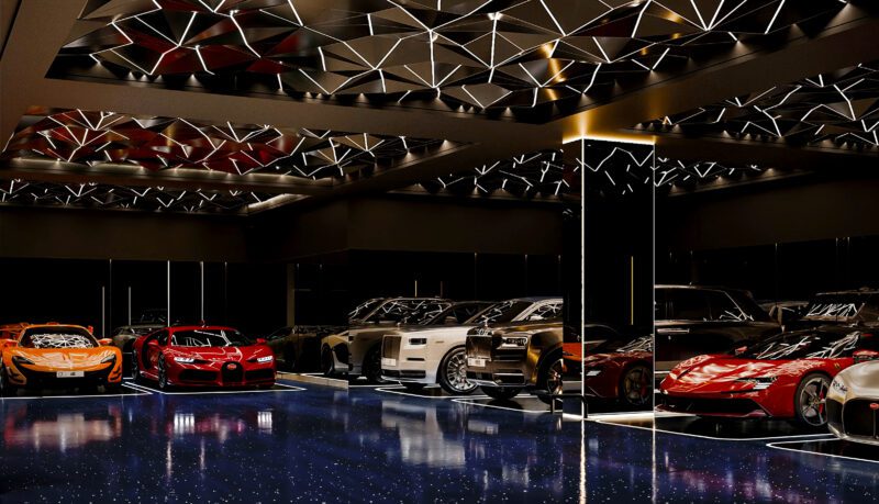 A modern, well-lit garage at Aureum Estate with a glossy blue floor and luxury cars, including sports cars and SUVs, parked in rows under a geometric mirrored ceiling.