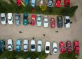 Aerial view of rows of classic cars, including Ferraris, parked in a lot in South Tyrol, Italy; people walk between them as part of the Ferrari Cavalcade. Cars are mostly red, white, silver, and green.