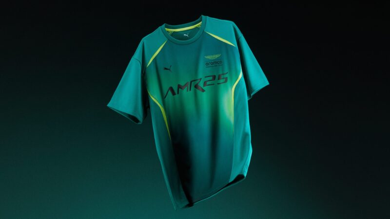 A green and yellow Aston Martin AMR25 T-shirt from the F1 Team Collection, featuring PUMA Motorsport and Aramco logos, displayed against a dark background.