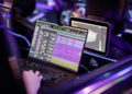 Person working on a laptop with audio editing software open, surrounded by digital screens and ambient LED lighting, inside a Mercedes that feels like a modern music studio.