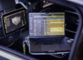 A laptop displaying audio editing software rests on a Mercedes Maybach car seat, with a mounted screen beside it showing a 3D audio visualization interface—transforming the vehicle into a rolling music studio.