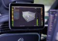 A Mercedes Maybach car seat back with its iconic logo and a mounted screen displaying a 3D data visualization—perfect for a mobile music studio. A laptop with code is also partially visible.