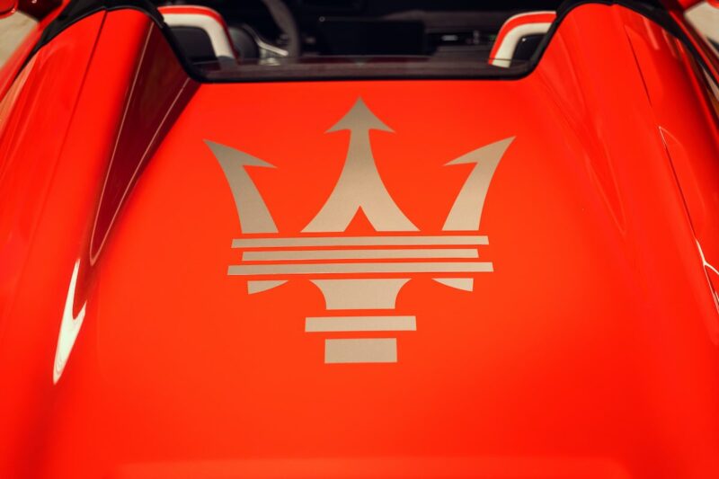 Close-up of a red car hood featuring a large silver Maserati trident logo in the center, as seen during the 2026 Maserati MCPura Cielo First Drive.