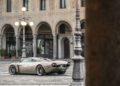 A silver Pagani Huayra Codalunga is parked in an empty cobblestone square, with ornate arches and street lamps in the background—an elegant scene fit for a Las Vegas Concours event.