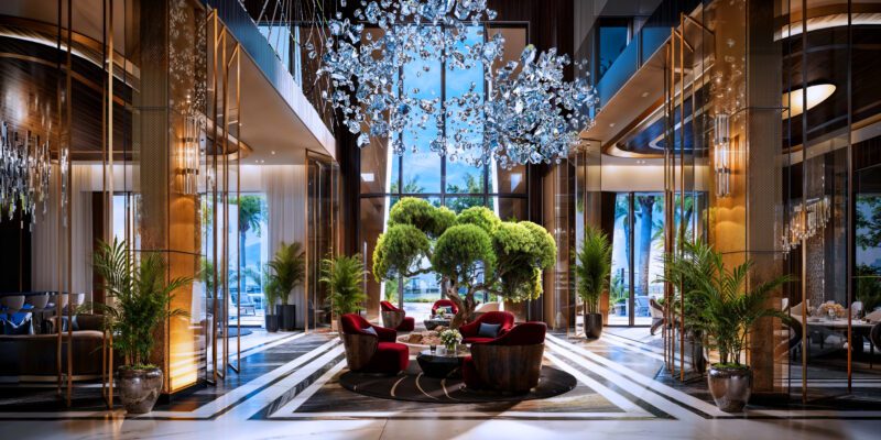 A luxurious hotel lobby at Aureum Estate with tall glass walls, modern chandeliers, red armchairs, green plants, and decorative trees, featuring abundant natural light and elegant decor inspired by Dubai Hills sophistication.