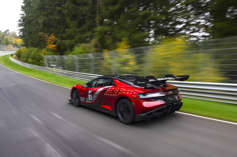 A red YANGWANG U9 electric hypercar with a large rear wing drives on a racetrack surrounded by trees and safety barriers, aiming for a Nürburgring record.