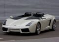 A white Lamborghini convertible sports car, styled by Lamborghini Centro Stile at 20: The Studio Behind Every Modern Bull, is parked on a paved surface in front of a corrugated metal wall.