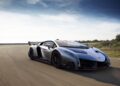 A metallic grey Lamborghini, designed by Lamborghini Centro Stile at 20: The Studio Behind Every Modern Bull, drives on a paved road under a blue sky, with greenery in the background.