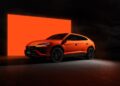 An orange Lamborghini Urus SUV is parked in front of a large, glowing orange rectangular backdrop in a dark setting, celebrating Lamborghini Centro Stile at 20: The Studio Behind Every Modern Bull.