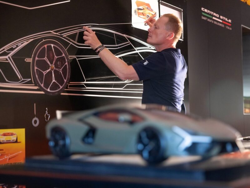 A person sketches a car design on a blackboard, with a model car displayed in the foreground—capturing the creative spirit of Lamborghini Centro Stile at 20: The Studio Behind Every Modern Bull.