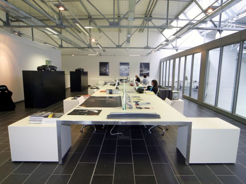 Modern open-plan office with large desks, computers, and a few people working; like Lamborghini Centro Stile at 20: The Studio Behind Every Modern Bull, it features large windows and sleek minimal decor throughout the space.