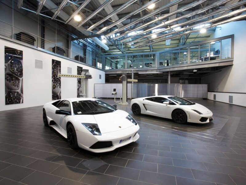 Two white Lamborghini sports cars are parked indoors on a tiled floor, highlighting the sleek design celebrated by Lamborghini Centro Stile at 20: The Studio Behind Every Modern Bull, with large windows and modern industrial architecture in the background.