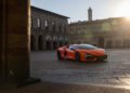 An orange Lamborghini sports car parked on a cobblestone plaza, with historic buildings and sunlight in the background, perfectly showcases how bold car colors can highlight the origins of Italian automotive design.