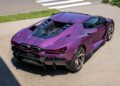 A purple Lamborghini Revuelto, a vibrant example of unique car colors in Lamborghini history, is parked on a paved surface near a crosswalk, viewed from above and behind.