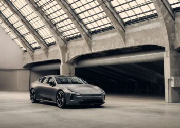 A matte grey Polestar 5 electric sports car is parked in a spacious, industrial-style building with large glass-panel skylights and concrete beams, ready for its cinematic debut in a film starring Alexander Skarsgård.