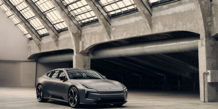 A matte grey Polestar 5 electric sports car is parked in a spacious, industrial-style building with large glass-panel skylights and concrete beams, ready for its cinematic debut in a film starring Alexander Skarsgård.