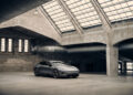 A sleek gray Polestar 5 sports car is parked in an empty industrial building with large windows, exposed brick walls, and concrete floors.