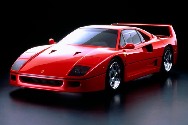 A red Ferrari F40 sports car is displayed in a studio setting with a black background, highlighting its aerodynamic design and rear spoiler—an iconic look often referenced in the Comparison: Ferrari F40 Vs Ferrari F50.