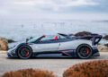 A Pagani Huayra Codalunga with red and black accents is parked on a coastal road, rocks and the ocean in the background beneath a cloudy sky—capturing the elegance found at events like the Las Vegas Concours.