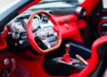 Close-up view of a luxury Pagani car interior featuring red leather seats, a wooden and red leather steering wheel, and a manual gear shift—an exquisite detail from the Huayra Codalunga at the Las Vegas Concours.