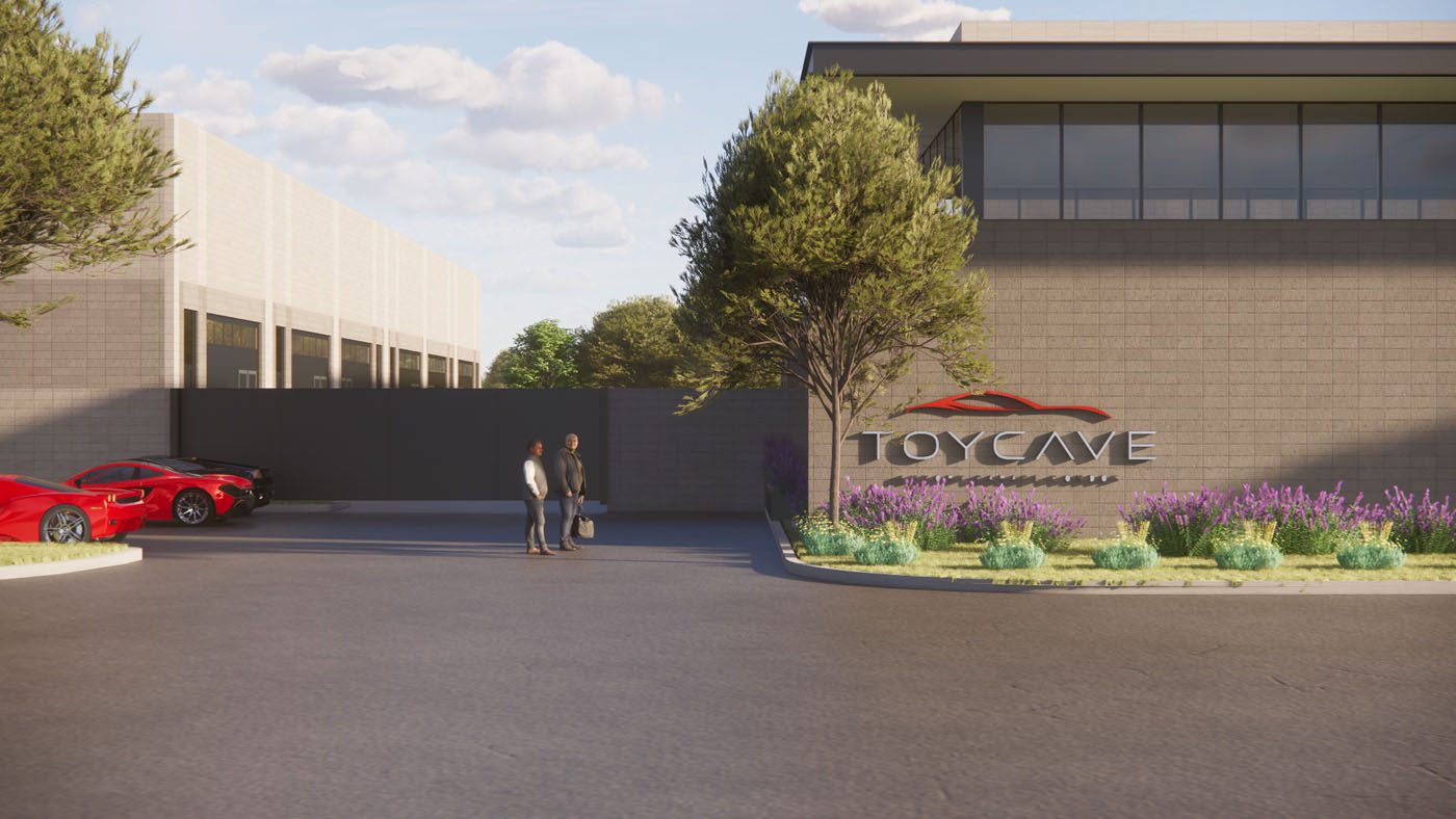 Two people stand outside a modern building with a "TOYCAVE" sign, parked sports cars, landscaped plants, and clear skies overhead.