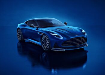 A blue Aston Martin DB12 S luxury sports car is parked on a glossy blue surface, photographed from the front left angle under bright lighting—an exquisite addition to the Super Tourers class.