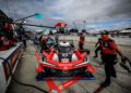 A red and black race car labeled 93 is serviced by crew members in the pit lane during the Petit Le Mans at a renowned track, with Rolex branding visible in the background.