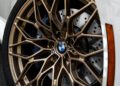 Close-up of a 2026 M2 Turbo Design Edition wheel, showcasing a bronze multi-spoke rim, blue brake caliper, and large ventilated disc, inspired by the legendary BMW 2002 Turbo, mounted on a white vehicle.